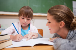 Image of Cute schoolgirl writing a while her teacher is talking